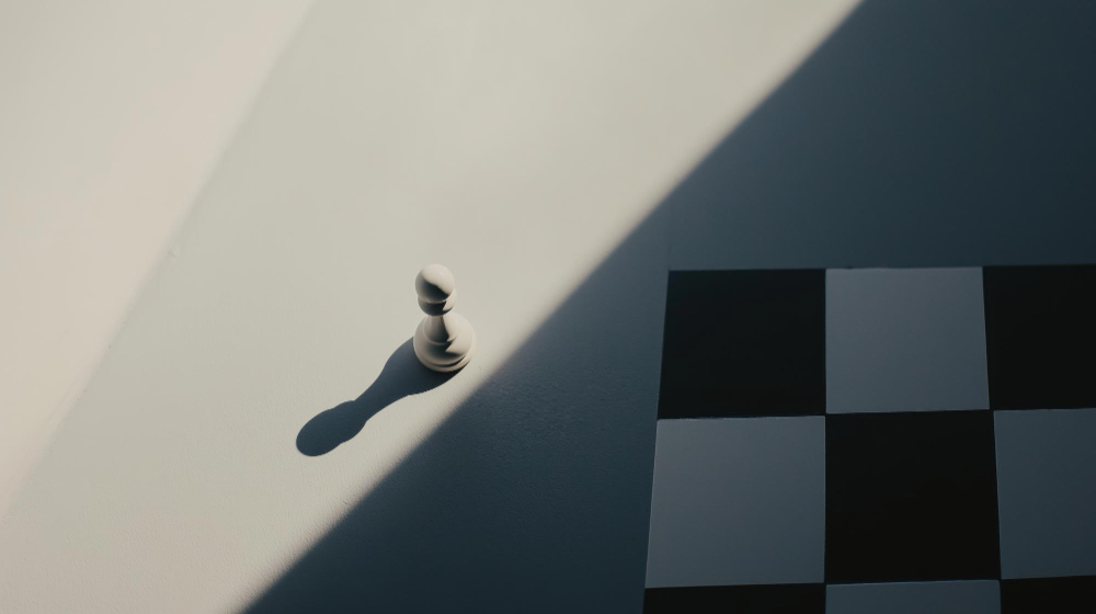 pieza de ajedrez fuera del tablero parcialmente iluminada con fondo de tablero en sombra